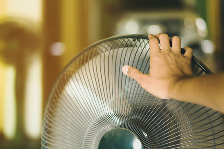 Hand of Young man touch and adjust  on front grills of electric fan for a good wind in his home in...