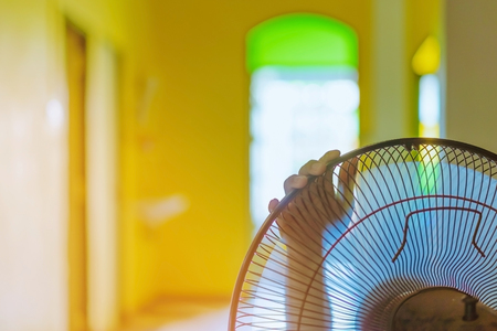 Hand of Young man touch and adjust  on front grills of electric fan for a good wind in his home in summer of april in Thailand.の写真素材