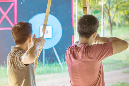 Tourists try to use a bow and arrow and shoot at a target in the amusement park.の写真素材