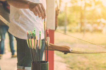 Tourists try to use a bow and arrow and shoot at a target in the amusement park.
