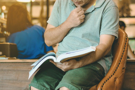 Asian man read a book in a coffee shop.