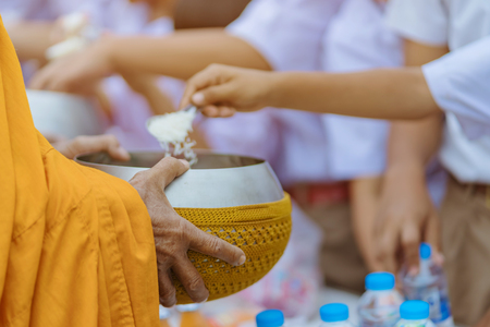 Teachers and students together make merit to give food offerings to a Buddhist monk on important religious days at school.の写真素材
