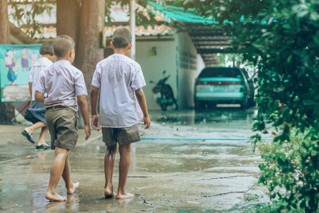 Boy students leave the classroom to walk on the street after heavy rain in the school.の写真素材