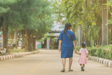 Mom and daughter pupil girl holding hand in hand on street go to the classroom together.の写真素材