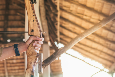Tourists try to use a bow and arrow and shoot at a target in the amusement park.