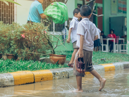 Boy students leave the classroom to walk on the street after heavy rain in the school.の写真素材
