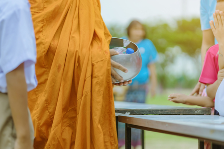 Teachers and students together make merit to give food offerings to a Buddhist monk on important religious days at school.の写真素材