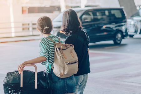 Passengers with big roller luggage stand to wait for the car to pick up at airport arrival terminal.の写真素材