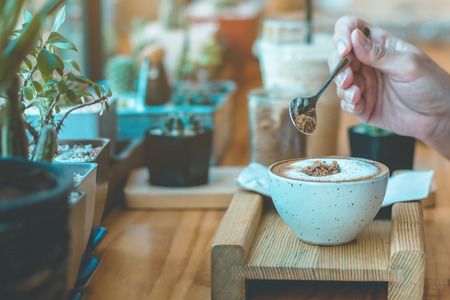 Woman pouring sugar into a white cup of coffeeの写真素材