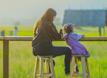 Mom and daughter sit for resting and waiting for time to take photos of the sunset on the farmer's balcony in the rice fields.の写真素材