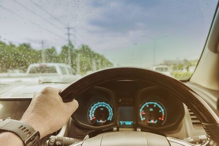 One hand of a driver on steering wheel of a car with speed and  raindrops on the windscreen in a rainy day. Dangerous driving car concept.の写真素材