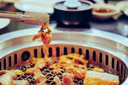People grilling meat on a smokeless barbecue grill in a restaurant. Selective focus on tongs.の写真素材