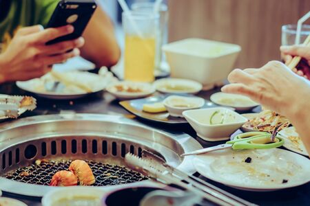 People grilling meat on a smokeless barbecue grill in a restaurant. Selective focus on shrimps.の写真素材