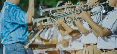 Male student with friends blow the trumpet with the band for performance on stage at night.の写真素材