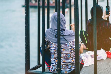 Back view of Muslim women relax and admire the beautiful scenery in the evening on The Bridge of the River Kwai in Kanchanaburi, Thailand.の写真素材