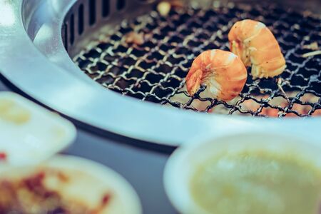 People grilling meat on a smokeless barbecue grill in a restaurant. Selective focus on shrimps.の写真素材
