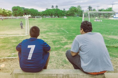Back view of male parents cheering their childrens playing football in school.の写真素材