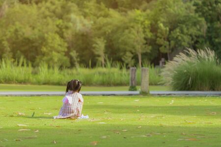 A little girl in a pink skirt enjoys a relaxing time playing on the green lawn at the public park in the evening.の写真素材