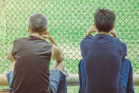 Back view of male parents cheering their childrens playing football in school.の写真素材