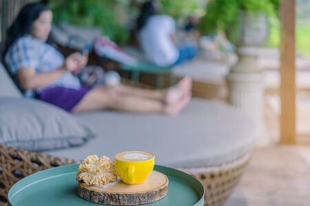 Hot coffee in a yellow cup and crispy lotus blossom cookie for relax time on wooden board at the balconyの写真素材