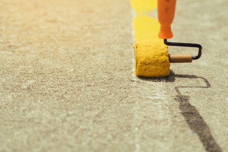Male students use small paint rollers to paint yellow lines on the cement floor for Sepak Takraw training.の写真素材