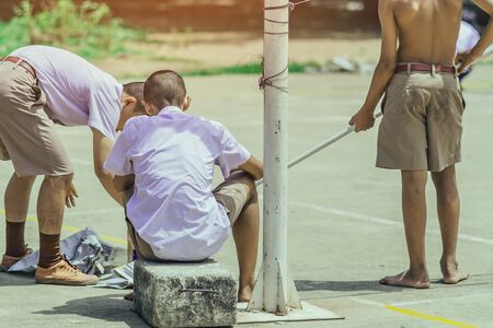 Male students use small paint rollers to paint yellow lines on the cement floor for Sepak Takraw training.の写真素材