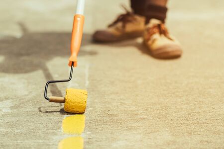 Male students use small paint rollers to paint yellow lines on the cement floor for Sepak Takraw training.の写真素材
