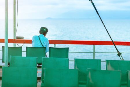 Asian man sits near baluster of ferry for relaxing and look at the ocean and island.の写真素材
