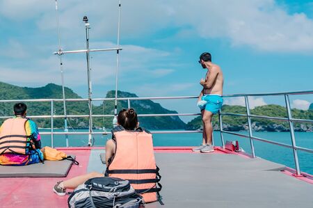 Tourists relaxing on boat deck and looking to the beautiful tropical island on hot sunny day.