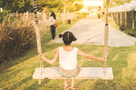 Back view of young girl sit on swings for wait her mom in the organic grapes farm.の写真素材