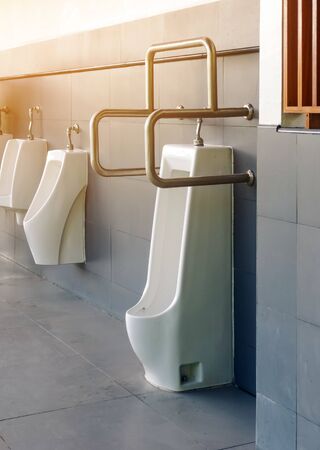 Clean and modern public men toilet with friendly design for people with disability or elderly with stainless steel handles and all white ceramic urinals row with automatic sensor flushing in gas station. Selective focus on stainless steel handles.の写真素材