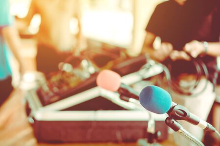 Two microphones with blue and red sponges placed on a stand with earphones on the table with blur image of the audio technician was installing and testing the sound system in the background.の写真素材