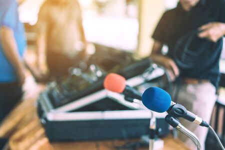 Two microphones with blue and red sponges placed on a stand with earphones on the table with blur image of the audio technician was installing and testing the sound system in the background.の写真素材