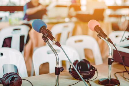 Two microphones with blue and red sponges placed on a stand with earphones on the table with blur...