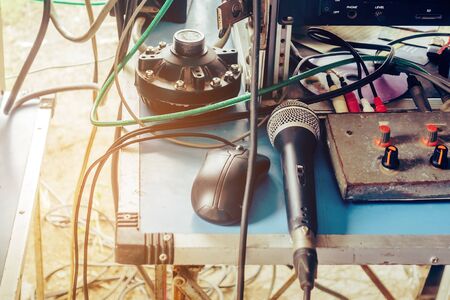 An old black condenser microphone and a black mouse placed on an audio control table with a tangled cable for used in outdoor announcements.の写真素材