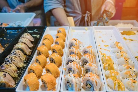 Rows of japanese sushi food. Maki ands rolls with tuna, salmon, shrimp, crab and avocado. Top view of assorted sushi in black plastic container being sale at market. Selective focus.の写真素材