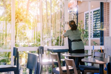 Back view of maid closes the glass window to turn on the air conditioner in the coffee shop.の写真素材