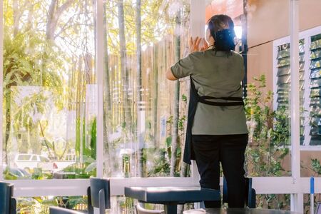 Back view of maid closes the glass window to turn on the air conditioner in the coffee shop.の写真素材