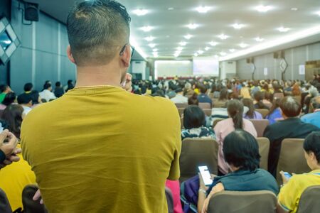 Backside view of spectators standing in a gathering in the back of auditorium full of people. Selective focus.の写真素材