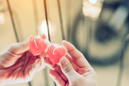 A red heart shaped candle in a woman's hand with candlelight in many small glass cups. A valentine's day background.の写真素材