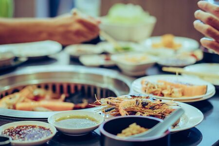 People grilling meat on a smokeless barbecue grill in a restaurant. Selective focus on shrimps.の写真素材
