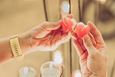 A red heart shaped candle in a woman's hand with candlelight in many small glass cups. A valentine's day background.の写真素材