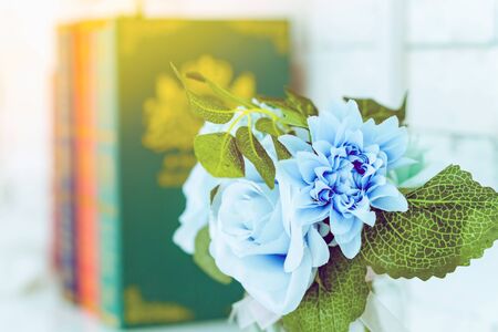 Beautiful artificial blue roses in glass vase on a white table with blured image of three books in the background.の写真素材