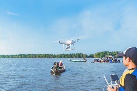 Young man in blue and yellow life vest controlling a drone to take pictures of ocean coast with tourists while traveling on a raft in the sea. Hands holding drone remote controller.の写真素材