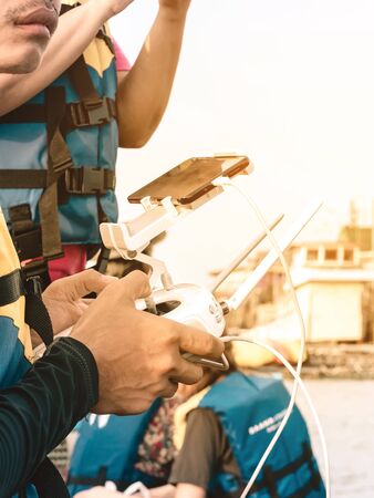 Young man in blue and yellow life vest controlling a drone to take pictures of ocean coast with...