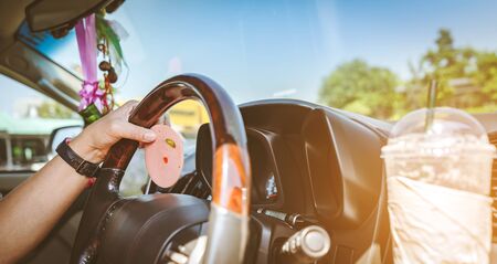 Hungry woman driving her car while eating bologna with ice coffee in the traffic. Selective focus on...