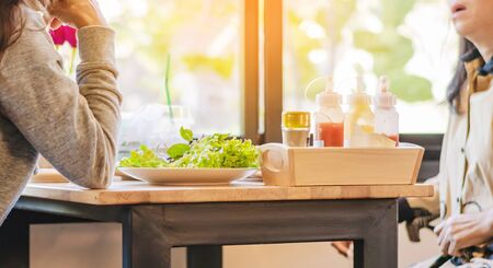 Happiness woman and friend talk and eat salads on the table in restaurant. Selective focus on lettuce.の写真素材