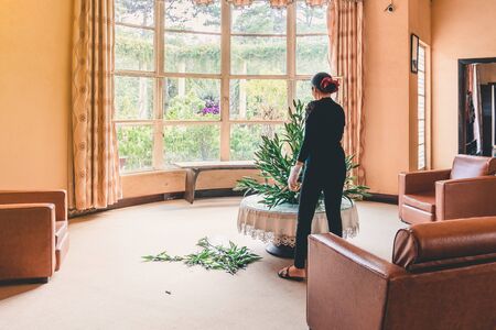 Female florist in black shirt arranging with bunch of lilies in the living room for a night time...