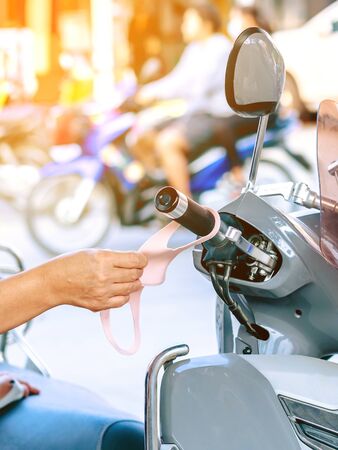 Hand of woman is picking a mask that is hung on a motorcycle handle to prevent germs (Covid-19) on roadside in the city. Corona virus protection concept.の写真素材