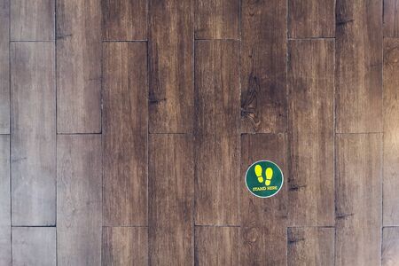 STAND HERE foot sign or symbol on the wooden floor in coffee shop. Coffee shop set foot sign for social distancing to order coffee and wait to take home.の写真素材